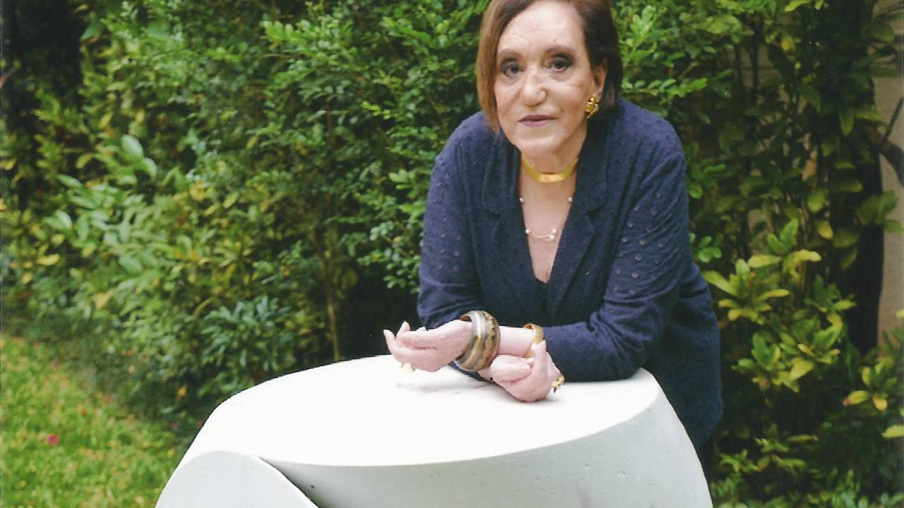 Senhora posa apoiada em obra branca semelhante a mesa