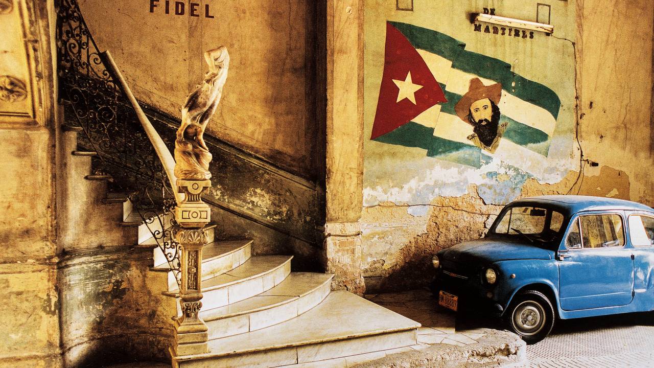 Escada à esquerda, carro azul antigo à direita e pintura da bandeira de Cuba na parede
