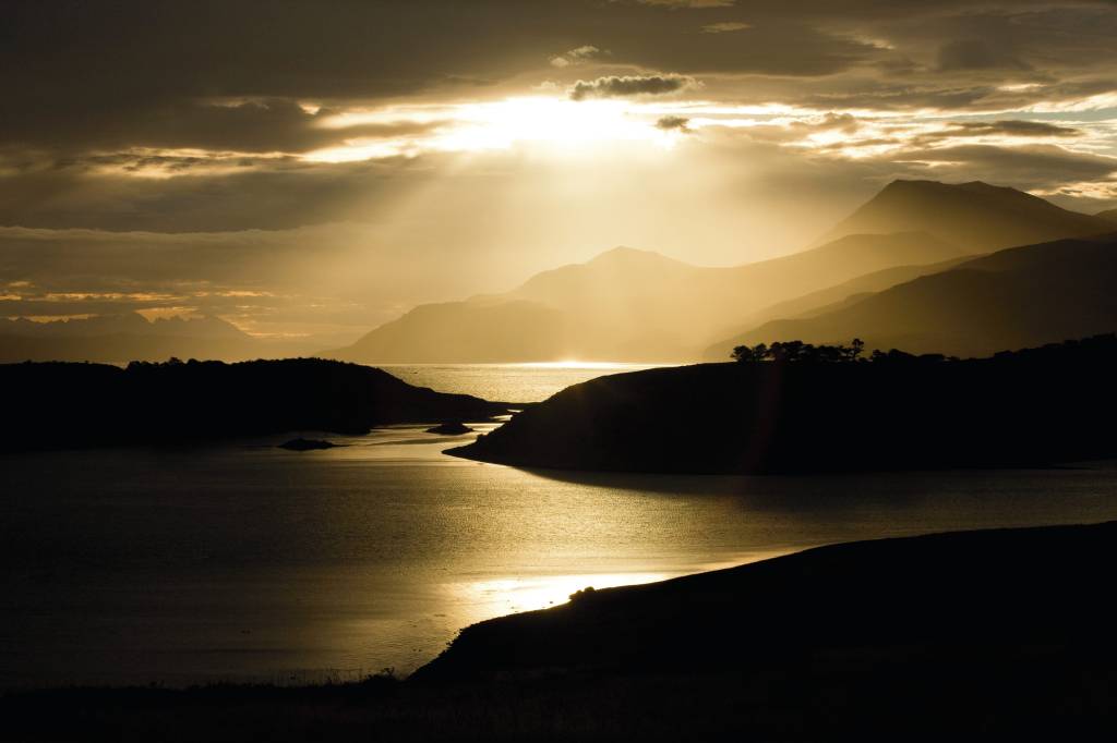 OKPatagonia retocada (1)-1 Cenário escuro com luz do sol batendo em grande lago envolto por montanhas