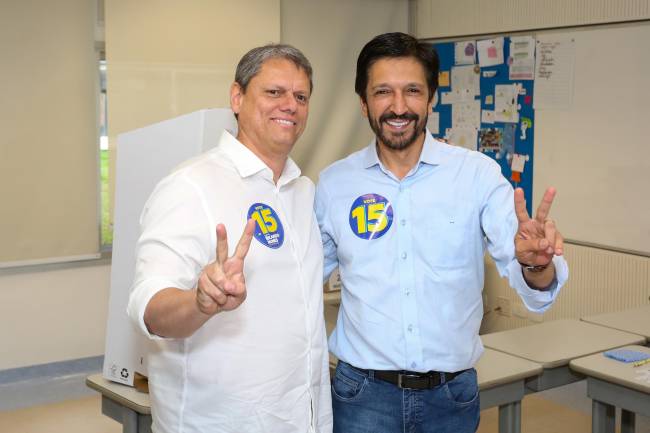 Duas pessoas sorrindo em sala de aula que acontece a votação