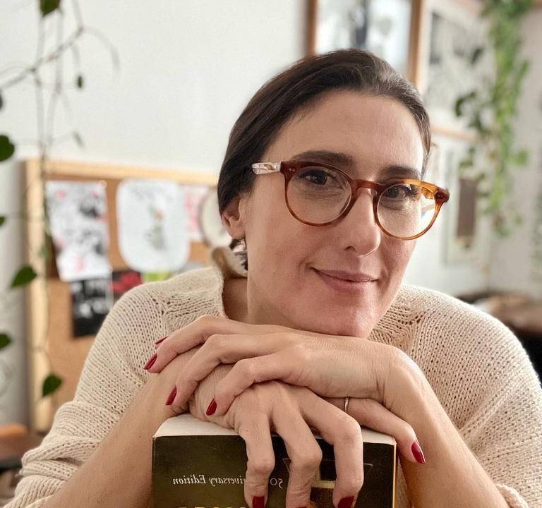 Mulher olhando pra câmera segurando um livro e sorrindo