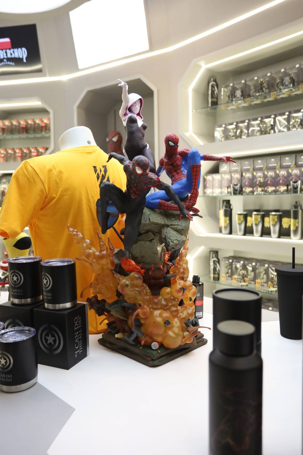 IMG_9413 Colecionável do Homem-Aranha no centro de uma loja com camiseta amarela à esquerda e canecas ao redor