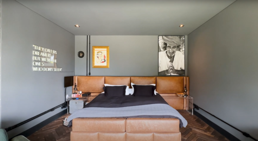 Quarto Cama king size com sofá marrom claro à frente e parede cinza ao fundo