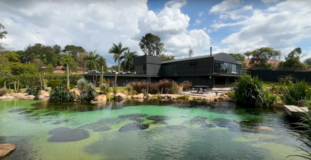 Lago esverdeado com rochas e casa preta ao fundo