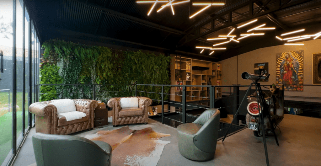 sala 1 segundo andar Sala de estar com poltrona verde moderna e sofás em tons claros. Ao fundo, parede esverdeada se assemelha a plantas suspensas