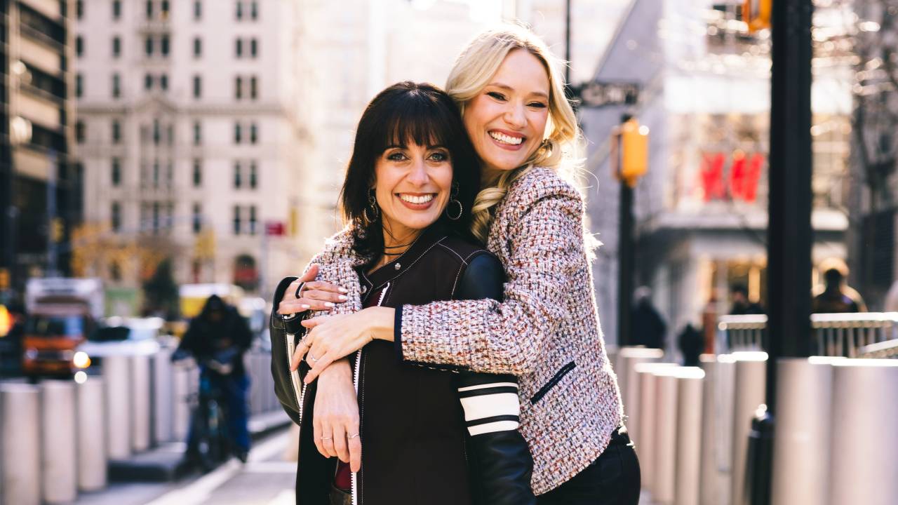 Morena e loira se abraçam em calçada de avenida larga de NY