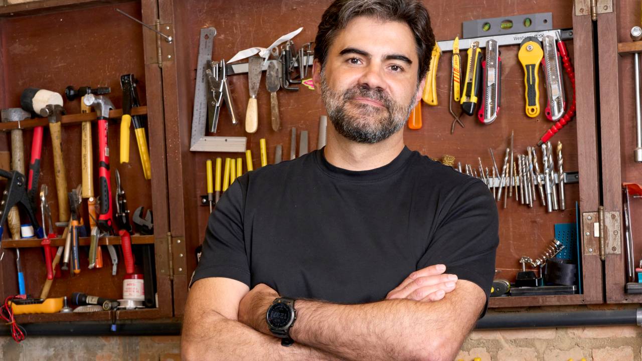 Homem branco de barba de braços cruzados em área de ferramentas