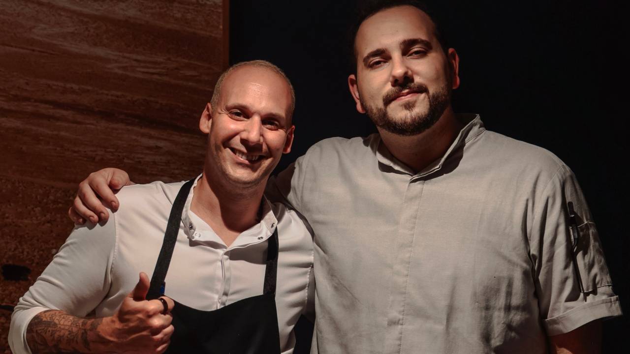 A foto traz dois homens vestido de dólmã e abraçado, os chefs Luiz Filipe Souza e Tomás Treschanski