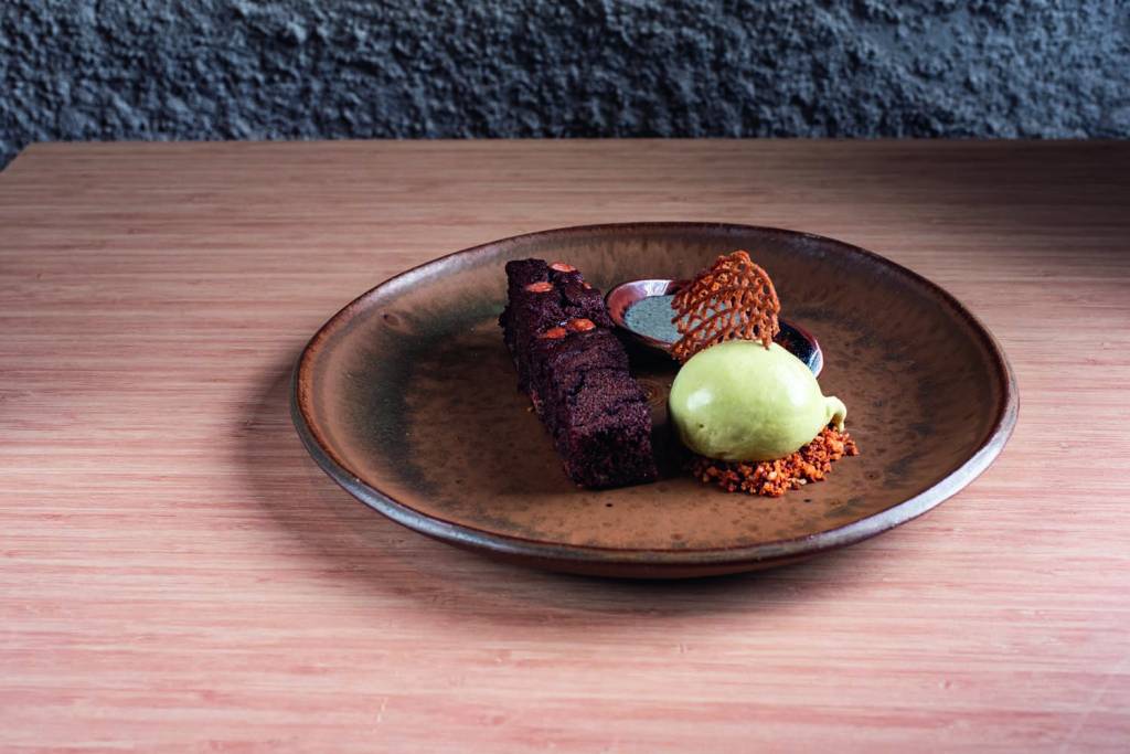 Kureiji – – Mochi brownie de banana e chocolate rubi com calda de gergelim preto e sorvete de pistache e matchá 033.jpg Sorvete com doces em prato marrom escuro