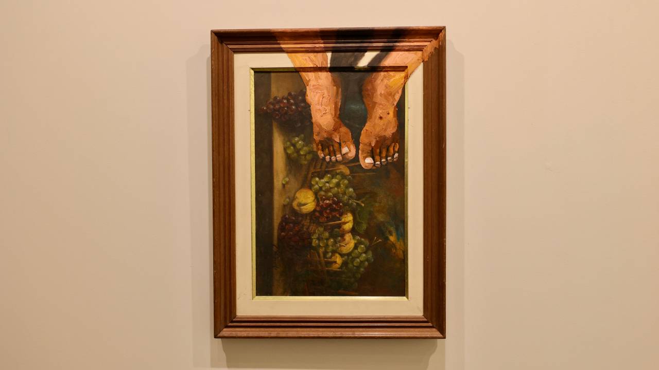 Quadro com pés no canto, a pintura inclusive na moldura, e frutas abaixo