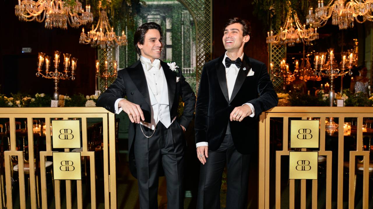 Dois homens brancos entre grade dourada, vestindo smokings