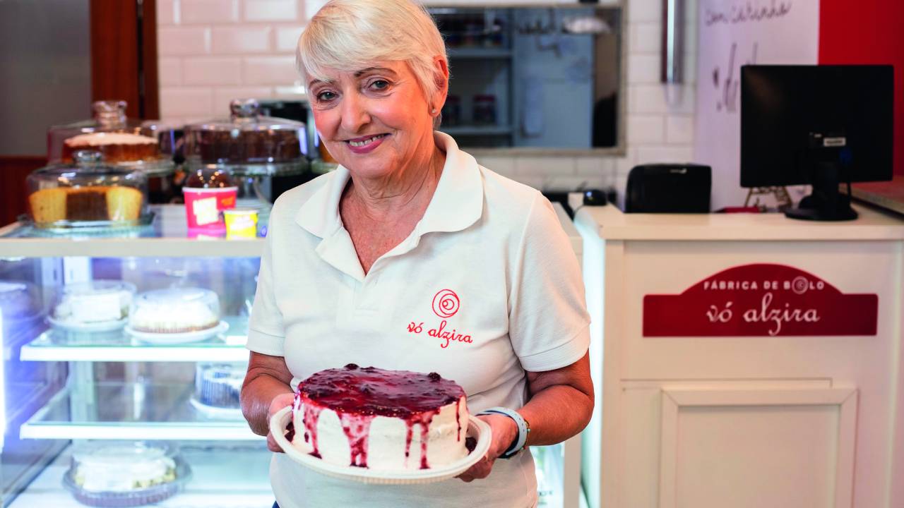 Mulher sorrindo e segurando bolo na frente da vitrine da loja
