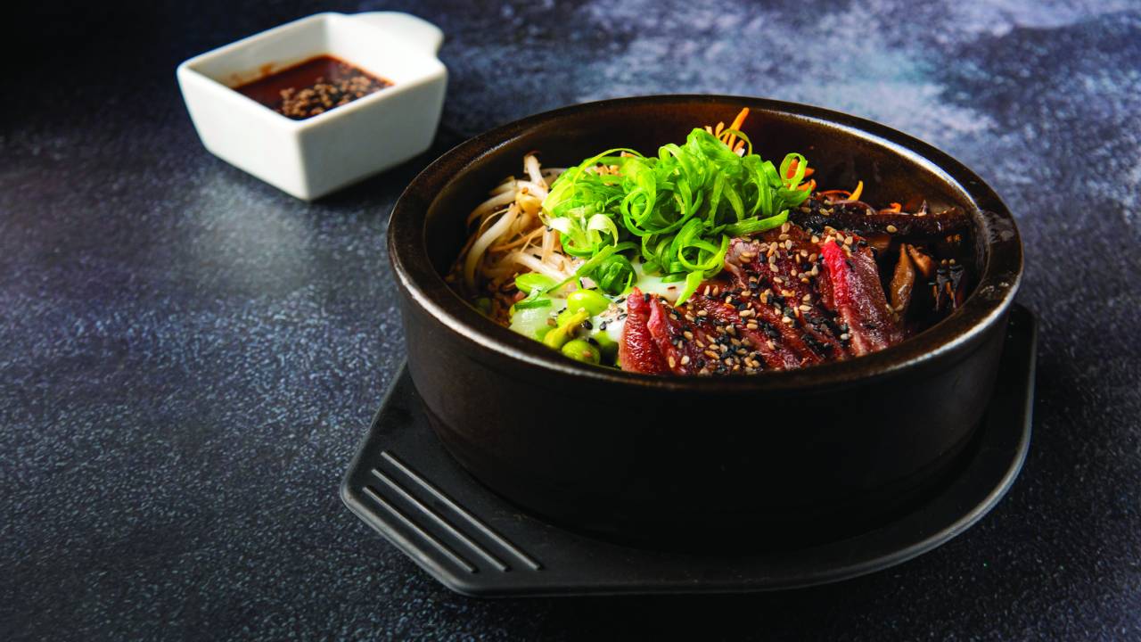 Prato com carne crua em panela preta e pote ao lado com molho