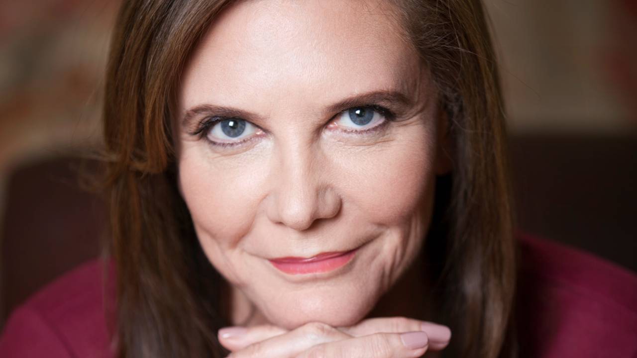 Moça branca posa com meio sorriso e as mãos no queixo
