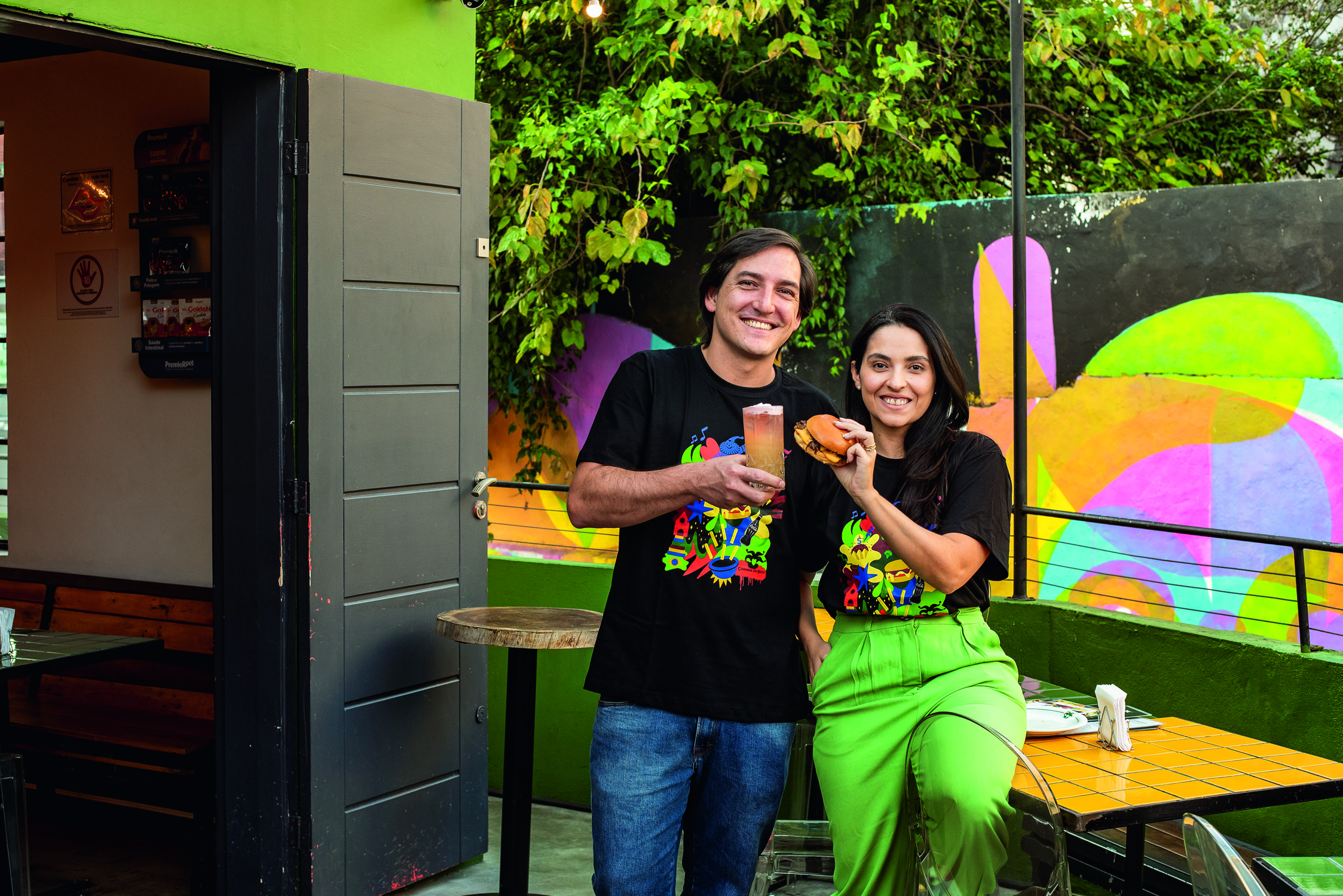 Duas pessoas sorrindo com hamb&uacute;rguer na m&atilde;o