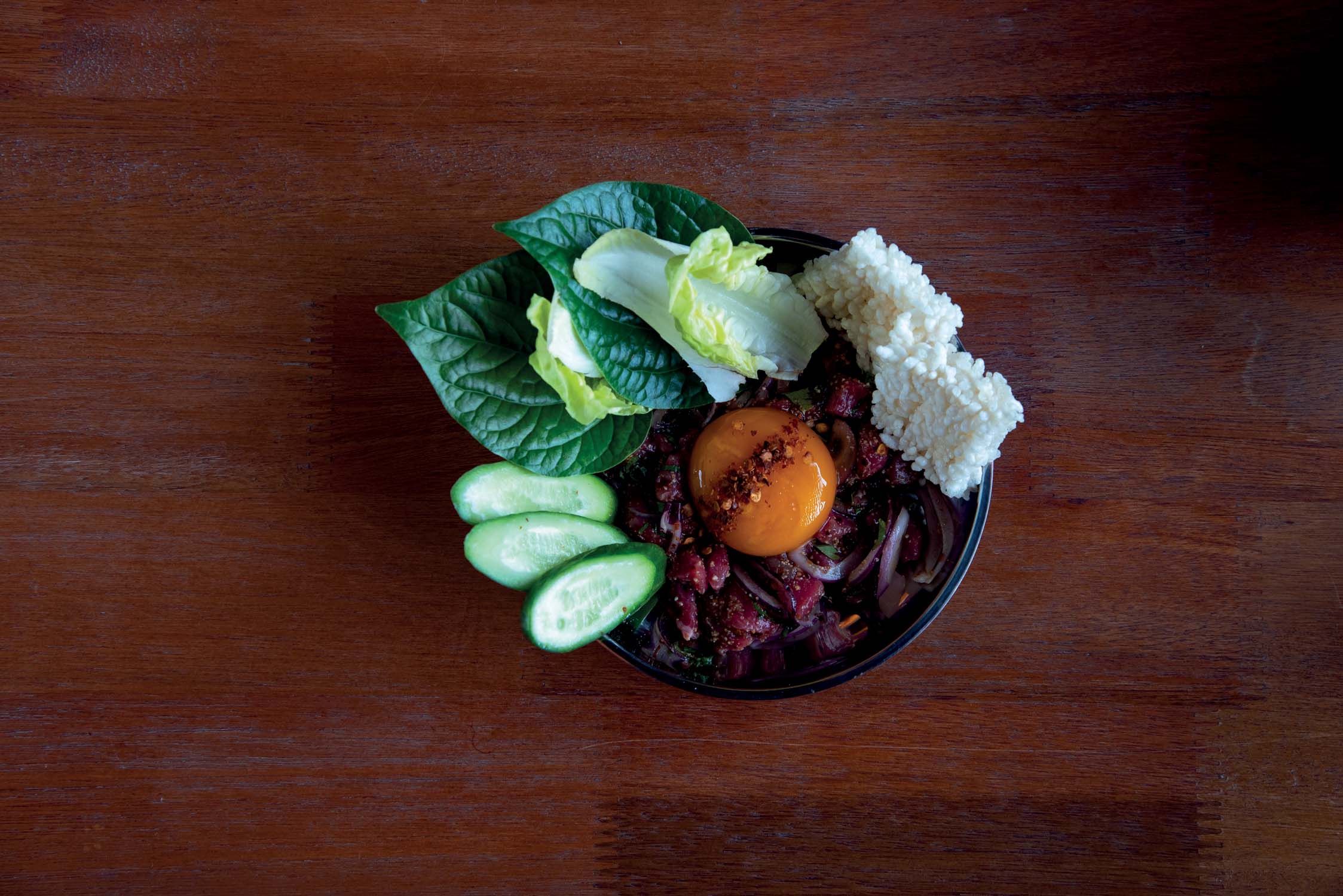 Koi neua: carne bovina marinada, com gema curada no molho de peixe ao lado de folhas