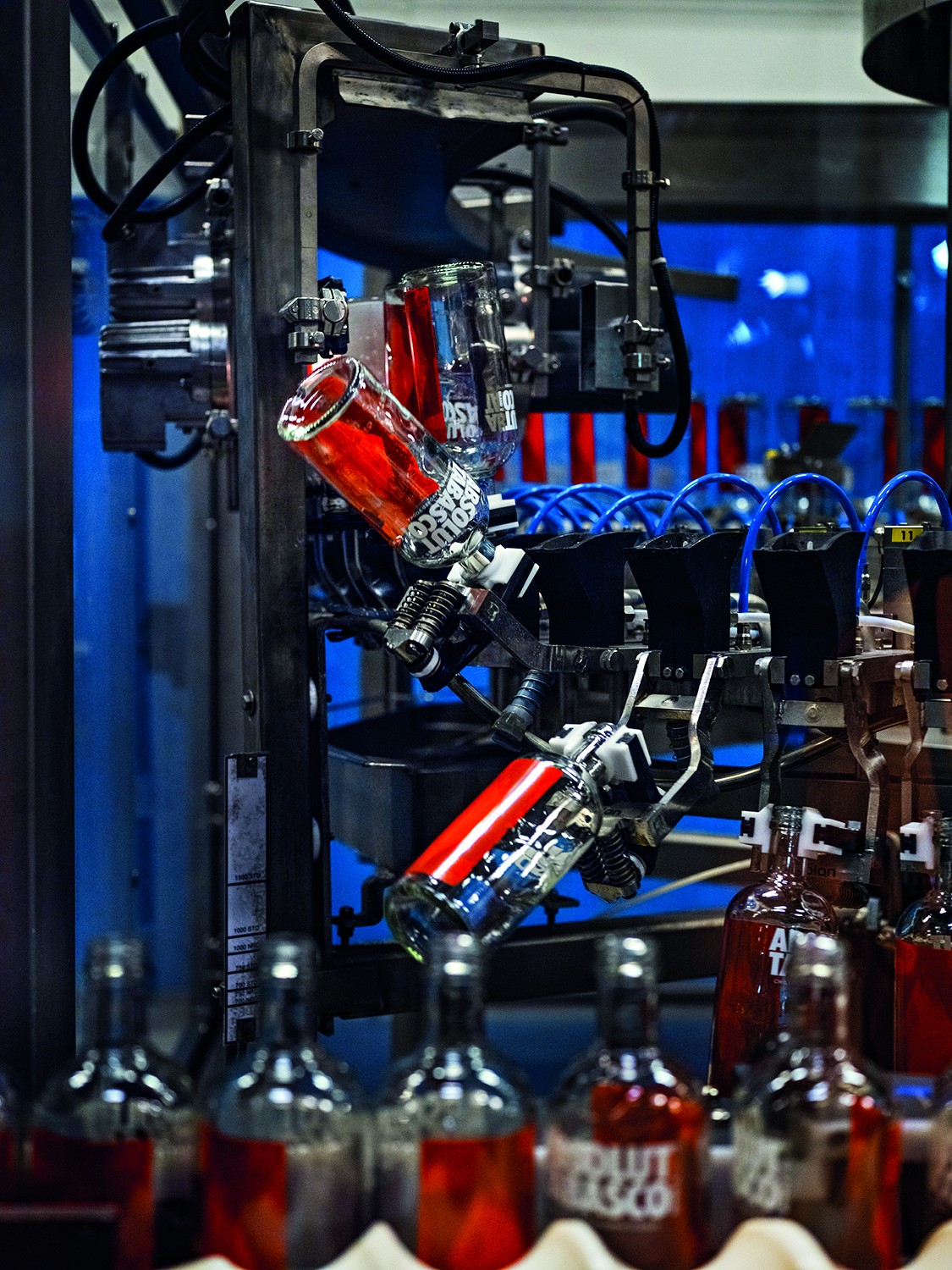 Garrafas de Absolut Vodka com r&oacute;tulos vermelhos sendo processadas em uma linha de engarrafamento industrial, com algumas de cabe&ccedil;a para baixo em m&aacute;quinas e outras alinhadas em primeiro plano
