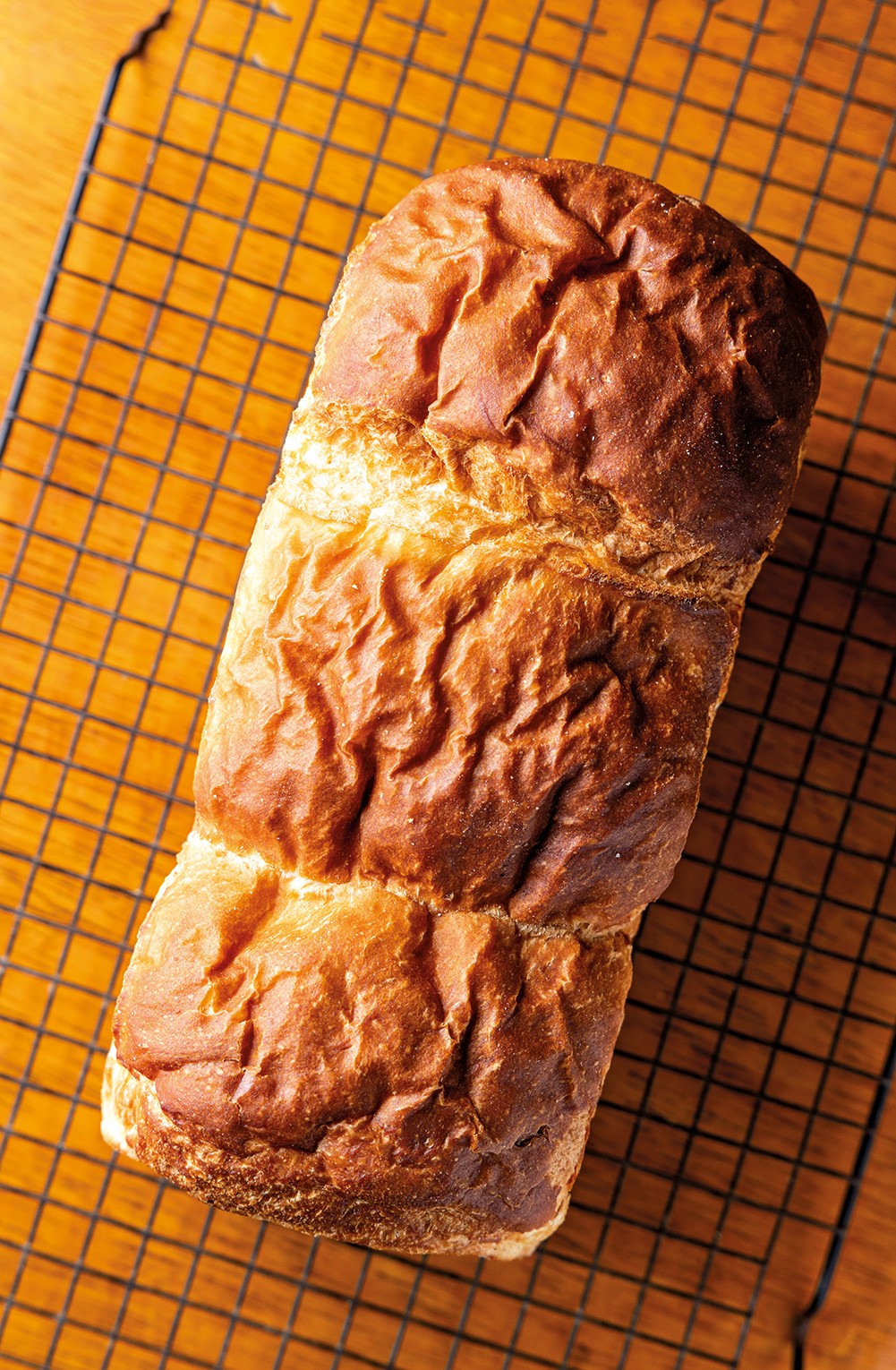 P&atilde;o caseiro rec&eacute;m-assado, com crosta dourada e rugosa, sobre uma grade de resfriamento preta em uma mesa de madeira clara