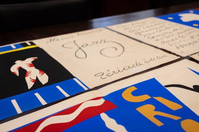P&aacute;ginas do livro Jazz de Henri Matisse, com ilustra&ccedil;&otilde;es coloridas em azul, vermelho, branco e preto, e textos manuscritos em franc&ecirc;s. Uma p&aacute;gina exibe a palavra Jazz em caligrafia elegante