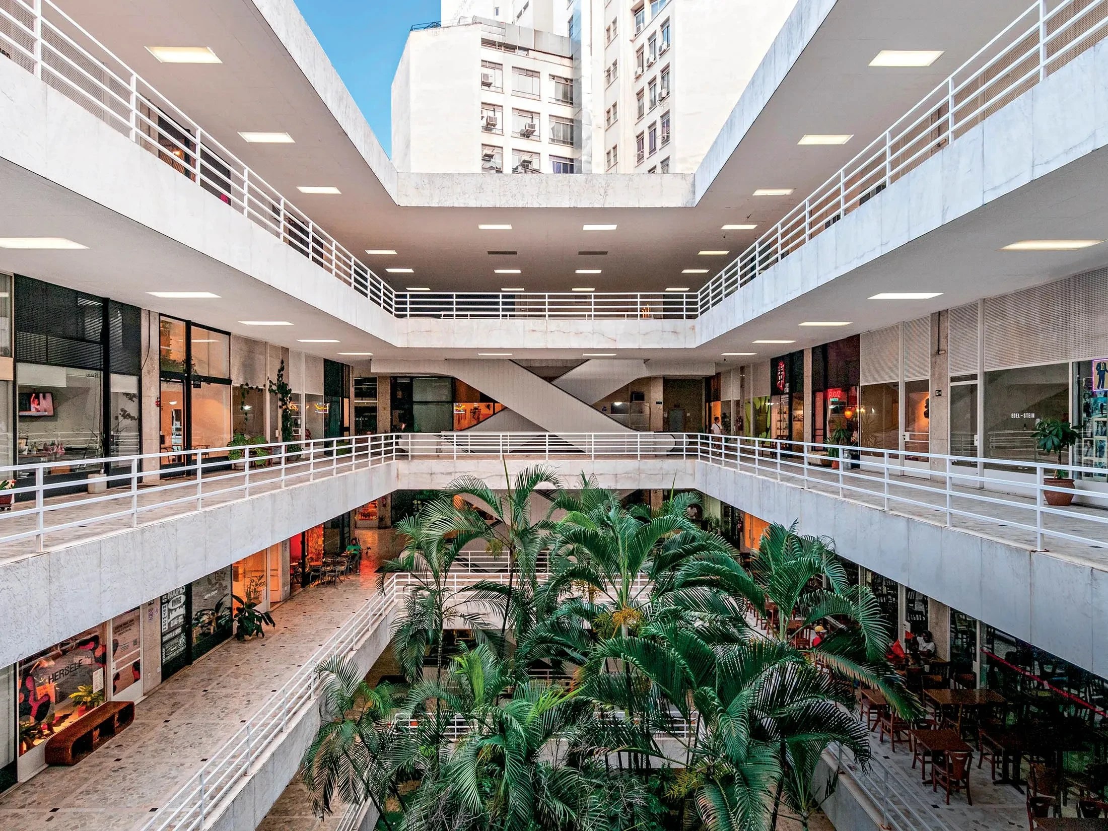 Interior moderno da Galerias do centro de SP com arquitetura minimalista, corredores abertos, plantas tropicais e áreas de convivência em um ambiente comercial iluminado e arejado.